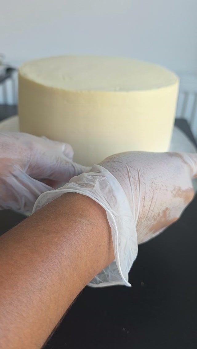 Gloved hands smoothing buttercream onto a fresh cake