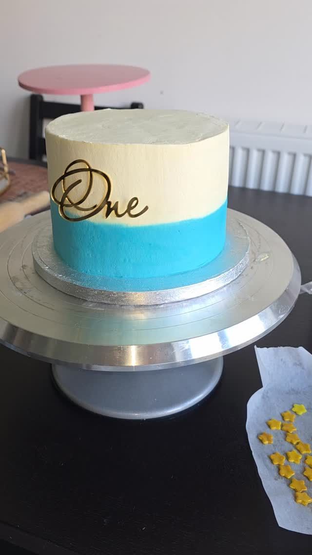 A blue and cream first birthday cake with a gold One topper